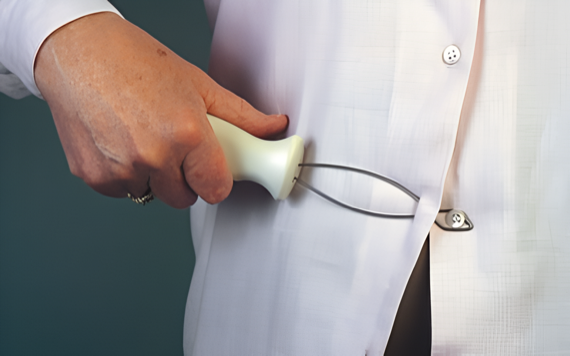 A person using a button hook tool to fasten a button on a white shirt, with their hand visible and a plain bluish-green background.