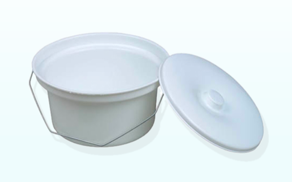 A white round container with a metal handle next to its matching lid, which has a small knob. They sit on a light background.