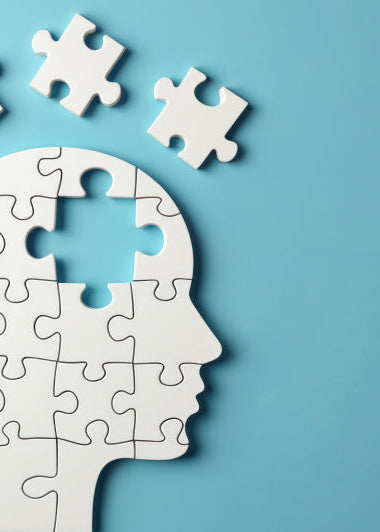 A human head silhouette made of white puzzle pieces on blue. One puzzle piece is missing from the top, with others floating above. Image