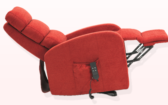 A red chair is fully reclined with a side pocket holding a remote. The cushioned backrest and footrest are supported by a black metal frame.