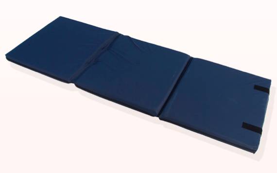 A person in a black shirt and grey pants is sitting cross-legged on a light grey couch, holding a tablet and looking focused.