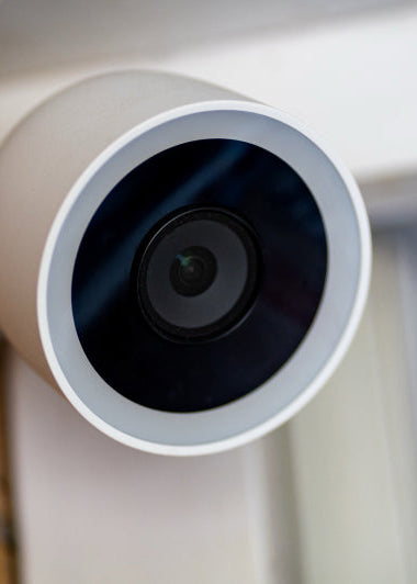 A round white security camera with a dark lens is mounted on a brick wall, angled downward to monitor the area. Image