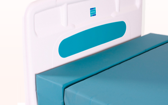 A hospital bed with a blue mattress and a white headboard featuring rounded corners and a blue accent under a small logo.