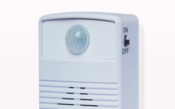 A white motion sensor with a round lens on front, switch labeled ON/OFF on side, and slits below; background fades from white to pink.