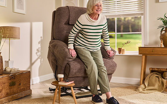 Older woman rising from a cushioned recliner chair in a bright living room, using the chair for support.