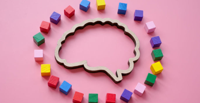 A wooden brain shape is surrounded by colorful cubes on a pink background, creating a playful and educational scene.