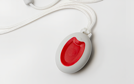 A white emergency call button with a red center and a looped white cord is placed on a white surface.
