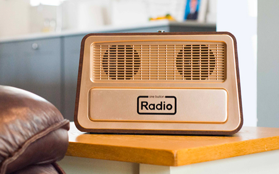 A vintage-style beige radio with two round speakers sits on a wooden table, blurred modern kitchen in the background.