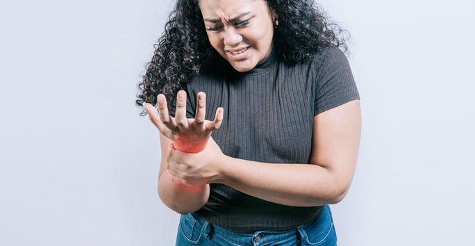 A woman with a distressed expression holds her right wrist, highlighted by a red glow to show pain, wearing a dark top and jeans.