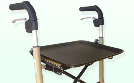 A light-colored mobility aid with black handles and brake levers, featuring a black tray table in the middle.