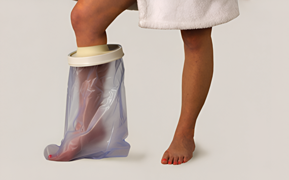 A person in a white towel has one leg in a clear cover, likely for water protection. The other foot is bare with red toenails.