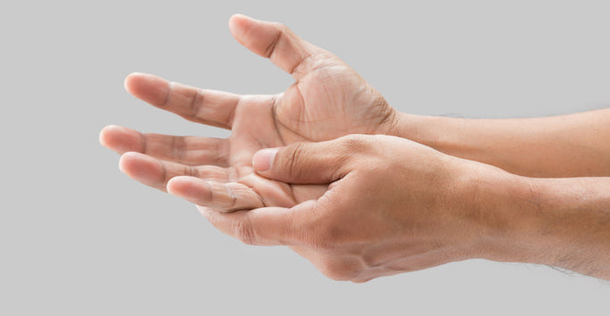 Two hands appear against a plain gray background, one gently massaging the other. The skin tone is light brown.