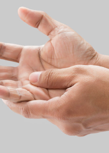 Two hands appear against a plain gray background, one gently massaging the other. The skin tone is light brown. Image