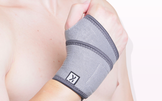 A person forms a fist wearing a gray wrist support with black stitching and a K logo. The background is plain and light-colored.