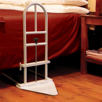 Homecraft Parnell Premier Bed Rail next to a red bed on wooden flooring with a nightstand holding magazines, side view.