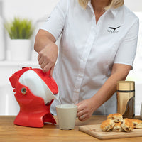 Red and white Uccello Kettle pouring hot water into a mug next to scones on kitchen counter, in use.