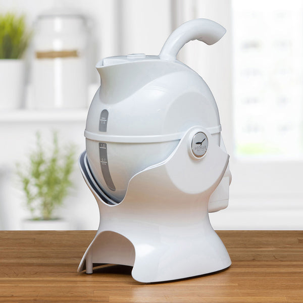 White Uccello Designs kettle with ergonomic handle on a wooden kitchen counter, angled side view.