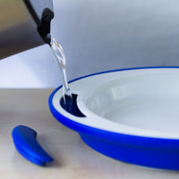 ORNAMIN Keep Warm Plate being filled with hot water from a kettle on a light surface, in use view.