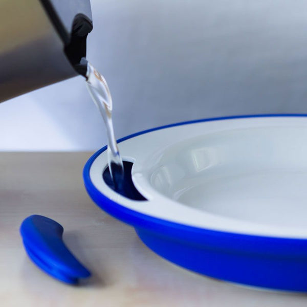 ORNAMIN Keep Warm Plate being filled with hot water from a kettle on a light surface, in use view.