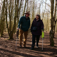 Older couple using red Medequip Ta-Da Chair walking seat sticks for support on a forest path, in use.