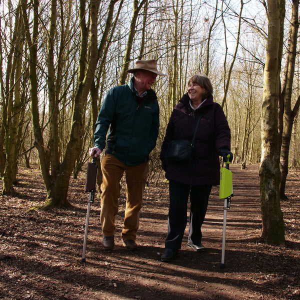 Older couple using red Medequip Ta-Da Chair walking seat sticks for support on a forest path, in use.