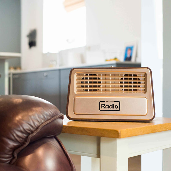 Ravencourt One Button Radio on a side table next to a brown leather chair in a bright modern living room, angled view.