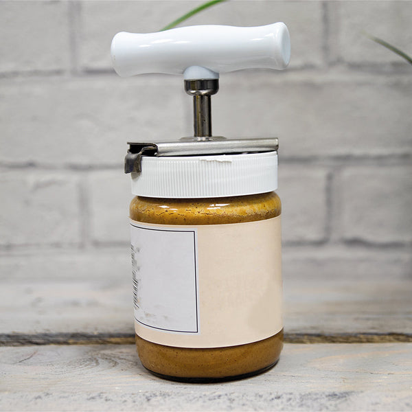 Aidapt jar opener with white handle on a table, plant blurred in background, front view.