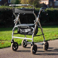 NRS 2 in 1 Rollator and Transit Chair with four wheels, padded seat and storage shown on park path, angled side view.