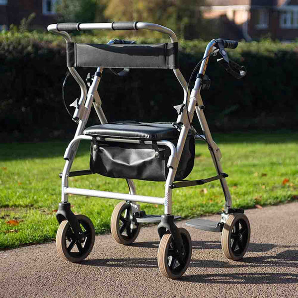 NRS 2 in 1 Rollator and Transit Chair with four wheels, padded seat and storage shown on park path, angled side view.