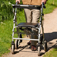 NRS 2 in 1 Rollator and Transit Chair with padded seat and storage basket used by a person outdoors on gravel, side view.