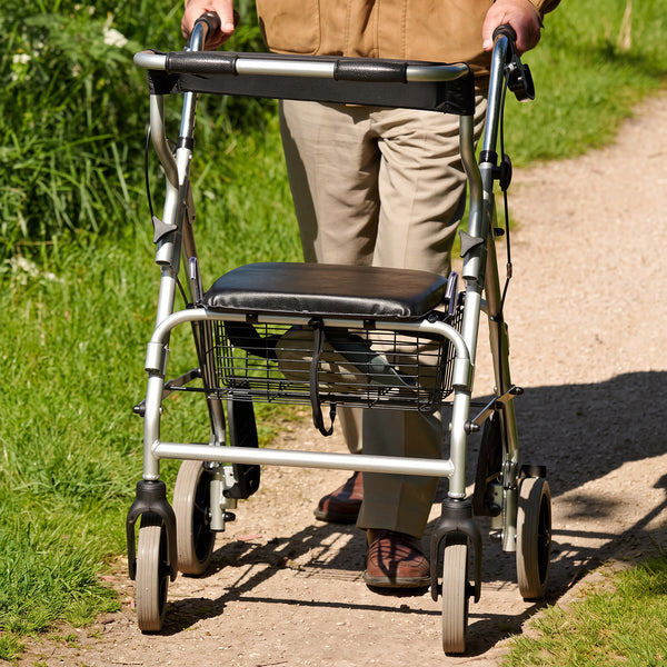 NRS 2 in 1 Rollator and Transit Chair with padded seat and storage basket used by a person outdoors on gravel, side view.
