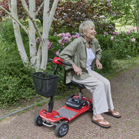 Older woman using a red Motion Healthcare eFly Travel Scooter in a garden, in use angle.