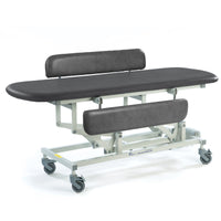 Black electric changing table with padded top, adjustable height, backrests and castor wheels, side view.