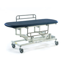 Dark blue electric changing table with padded top, metal frame, guard rails and wheels, height adjustable; side view.