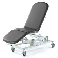 Dark grey three-section electric medical couch with wheeled metal frame, height adjustment controls visible, side view.