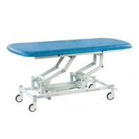 Hydraulic therapy hygiene table with blue padded top, white frame and four wheels, shown from side view.
