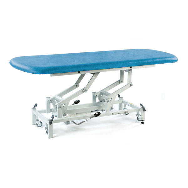 Hydraulic therapy hygiene table with metal frame, wheels, and adjustable sections, shown in a clinical setting, side view.
