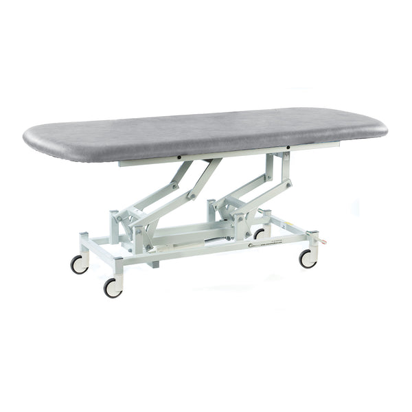 Light grey SEERS Medical electric therapy hygiene table with padded top, sturdy metal frame and castor wheels, side view.