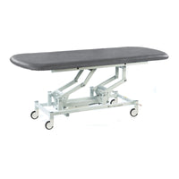Dark grey electric therapy hygiene table with height adjustment, padded top and wheels, side view.