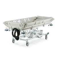 Hydraulic shower trolley with adjustable height, side rails, wheels and drainage hose, shown from the side.
