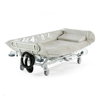 Padded hydraulic shower trolley with side rails, wheels, and hose attachment for hygiene, shown from a side angle.