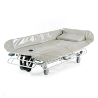 Grey padded hydraulic shower trolley with raised sides and wheels, waterproof surface, side angle.