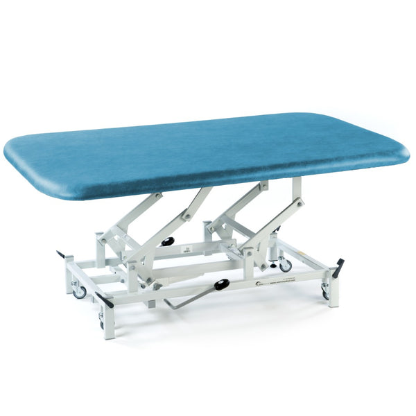 Blue cushioned SEERS Medical hydraulic therapy mat table with white frame and wheels, side view.