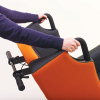 Person holding black handlebars on an orange and black Boston Healthcare mobility chair, in use, side view.