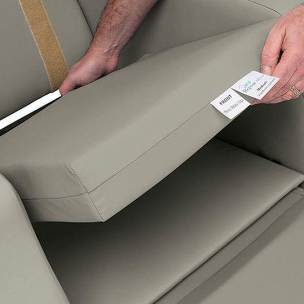 Removable seat cushion being lifted from Madison Healthcare Chair by Repose Seating, label visible underneath, close-up view.