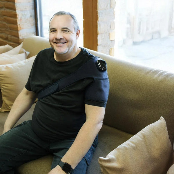 Man using Lifemax 3 in 1 Heated Vibration Massager and wearing shoulder brace on couch, in use view.