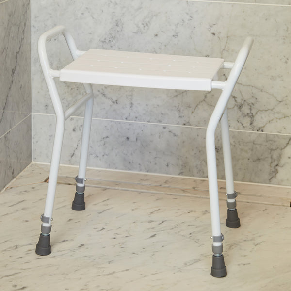 NRS shower stool with handles, metal legs and rubber tips on bathroom floor by tiled wall, front angle.