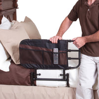 Stander Adjustable Bed Rail with storage pockets fitted to a bed, person holding remote control, in use side view.
