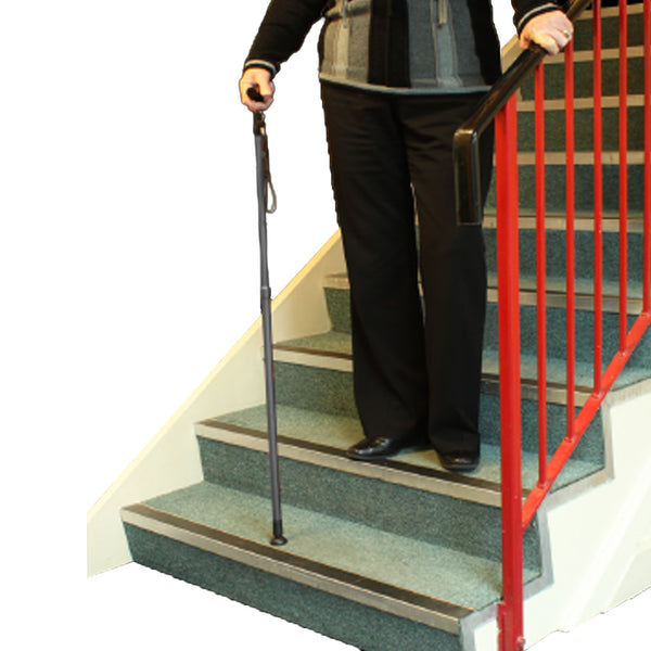 Lifemax Adjustable Walking Stick with non-slip rubber foot in use on carpeted stairs, person holding handrail, side view.