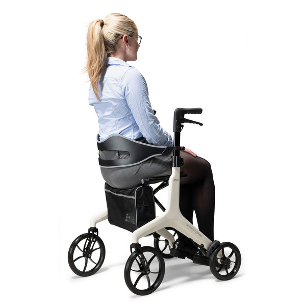 Drive AeroWalk Carbon Rollator in Buttercream with woman seated sideways, white background, side view.